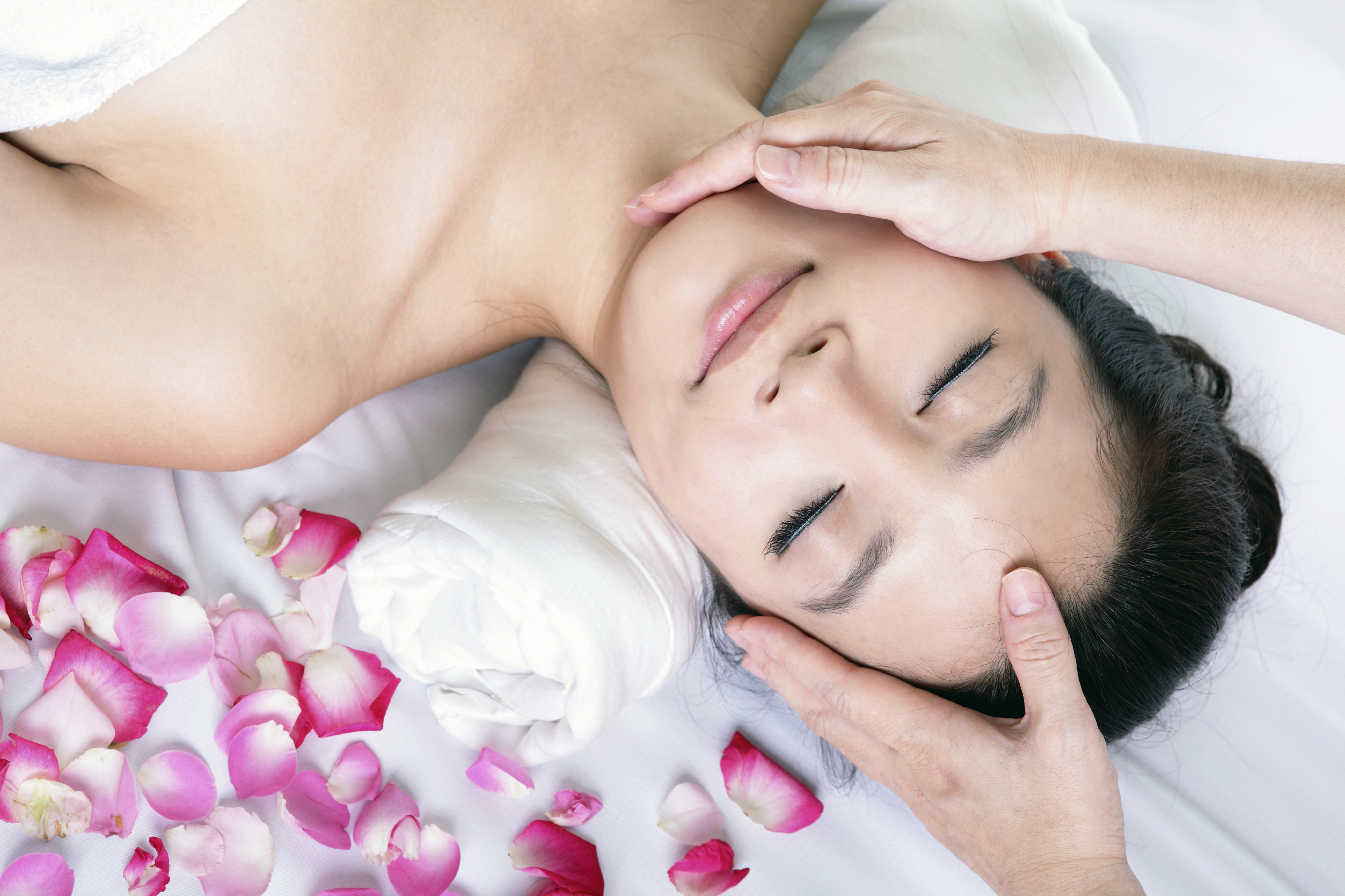 woman enjoy receiving face massage at spa with roses.