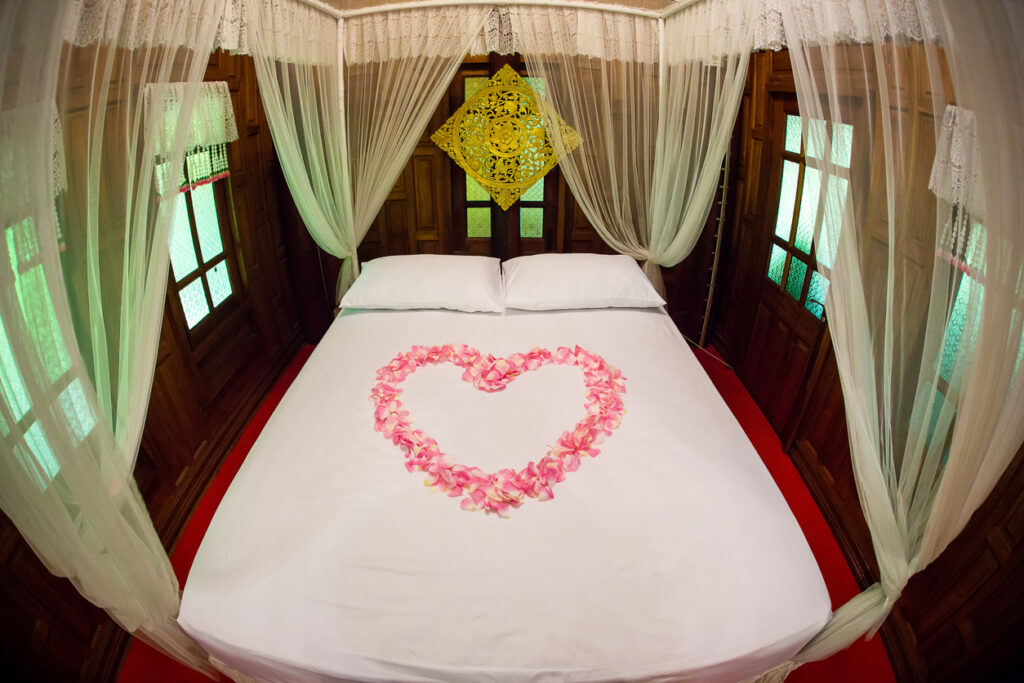 Heart shape from pink rose petals on the white bed. honeymoon suite room decoration. luxury suite. holidays with valentine theme.