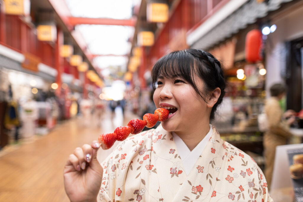 Japanese woman in kimono eating strawberry on shopping street