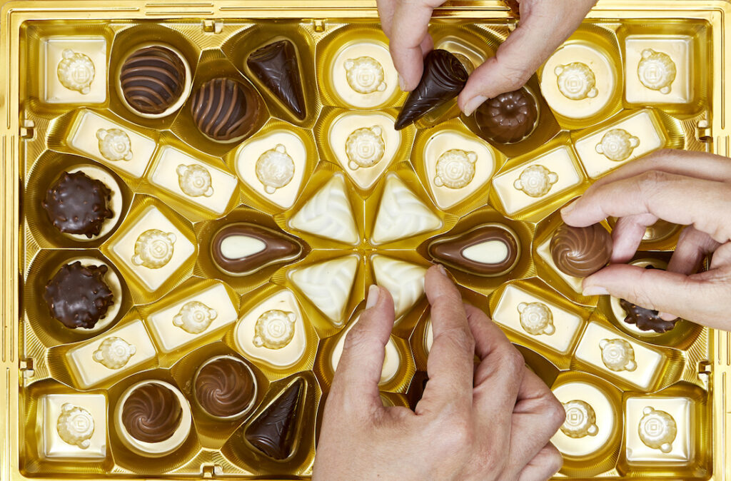people hands  holding eating  chocolate pieces from various type in golden box for valentine's day
